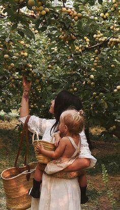 a woman holding two small children in her arms while picking fruit from an apple tree