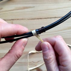 two hands holding wires connected to each other on top of a wooden table next to cords