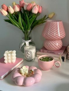 a table topped with pink vases and flowers on top of it next to books