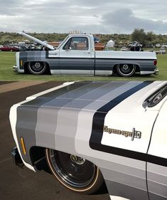 an old car parked in a parking lot with other cars behind it and another one on the grass