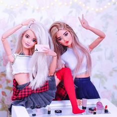 two dolls sitting on top of a table holding up their hands and taking a selfie