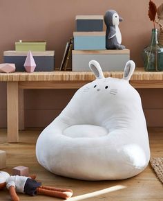 a white bunny bean bag chair sitting on top of a wooden floor next to toys