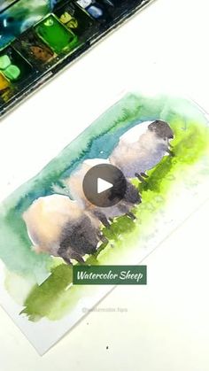 the watercolor sheep is sitting on the table next to the paintbrush and paper