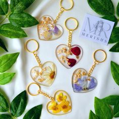 four heart shaped keychains with flowers and leaves around them on a white surface