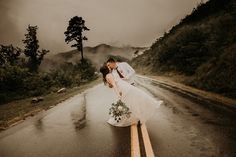 a bride and groom kissing in the middle of an empty road on a rainy day