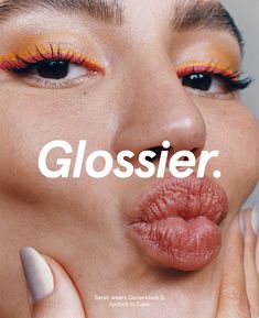 a woman with orange and yellow makeup has her hand on her face as if to say, glossier