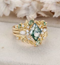 a gold ring with green and white stones on it, sitting next to some flowers