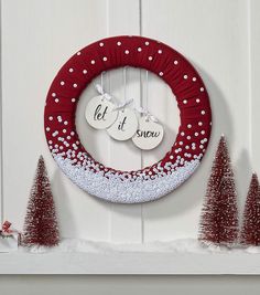 a christmas wreath with two ornaments hanging from it's side next to small trees