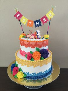 a multi layer cake decorated with colorful flowers and buntings on a wooden table