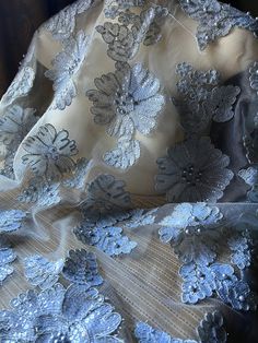 the back of a chair covered in blue and white lace fabric with flowers on it