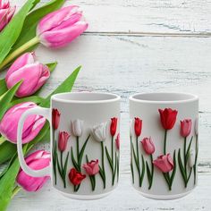 two mugs with flowers painted on them sitting next to some pink tulips