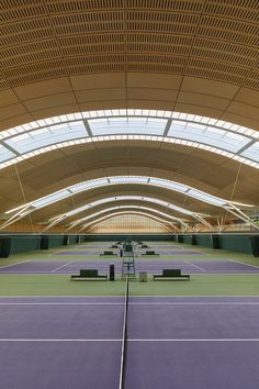 an empty tennis court with benches under a large roof over looking the court and sky