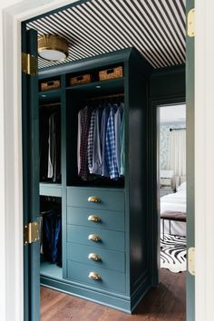 an open closet with clothes hanging on the doors and drawers, in front of a bed