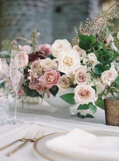 the table is set with white and pink flowers in vases, silverware, and wine glasses