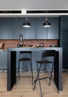 a kitchen with two stools and a table in front of the counter top that has three lights hanging above it