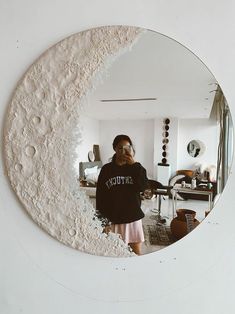 a woman standing in front of a mirror with the moon on it's side