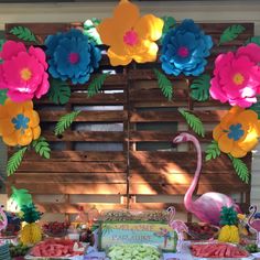 a table topped with lots of food covered in paper flowers and flamingos on top of it