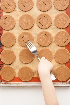 a person holding a fork over some crackers on a baking sheet with holes in it