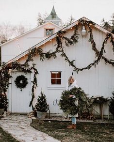 a woman standing in front of a white house with christmas wreaths on the door