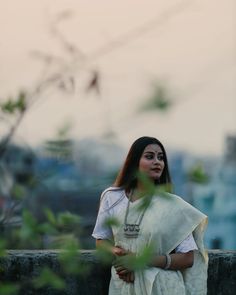 a woman standing in front of a tree with her hands on her hips and looking off into the distance