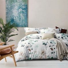 a bed with blue and white sheets in a room next to a plant on the floor