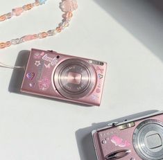 a pink camera sitting on top of a white table next to a beaded necklace