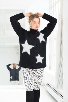 a woman standing in front of a mirror wearing black and white stars on her sweater