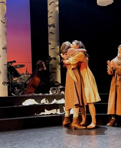 three people hugging each other on stage with musical instruments in the backgrouund