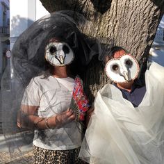 two people wearing masks standing next to a tree