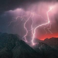 lightning strikes over mountains in the sky with purple and orange lighting on it's sides