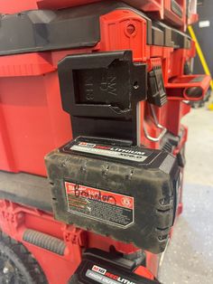 a red and black tool box on the back of a truck with two batteries attached to it