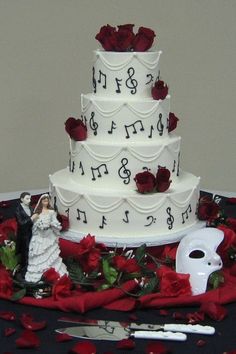 a three tiered wedding cake with red roses on the table next to knife and fork