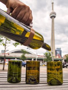 a person pours water into three glass cups on a wooden table in front of a tall building