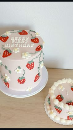 there is a pink cake with strawberries on it next to a small white cake