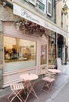 two pink folding chairs sitting in front of a store with flowers hanging from the windows