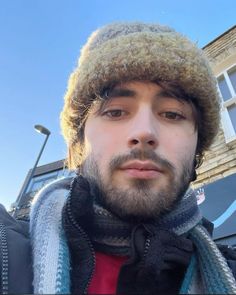 a man with a beard wearing a hat and scarf on top of his head while standing in front of a building