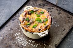 a baked dish is sitting on top of a black tray with sprinkled parmesan cheese and basil