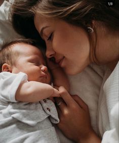 a woman holding a baby in her arms and kissing it's face with both hands