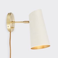 a wall lamp with a white shade on it's side and a gold arm