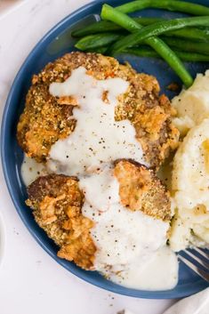 a blue plate topped with mashed potatoes and meat patties next to green beans