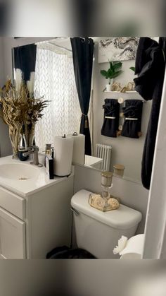 a white toilet sitting next to a sink in a bathroom under a window with black curtains