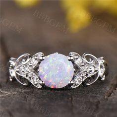 a white opal and diamond ring sitting on top of a piece of wood