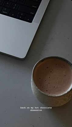 a cup of hot chocolate next to a laptop computer on a white table with the caption back on my first chocolate