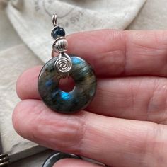 A small 20mm diameter donut gemstone, carved from AA quality Labradorite with blue flashes of colour. I have wrapped the natural gemstone in sterling silver wire, to create a spiral design on the bail, so i can hang it on to the black adjustable necklace cord. Natural healing crystal Jewellery.  A small labradorite adjustable pendant, wire wrapped in sterling silver wire.. A great gift for a teen. Chakra stone Jewellery. ADJUSTABLE LENGTH: Slide the knots from choker to chest length.  These are Round Labradorite Wire Wrapped Jewelry, Wire Wrapped Round Silver-plated Jewelry, Chakra Stones Jewelry, Donut Pendant, Adjustable Knot, Healing Crystal Jewelry, Sterling Silver Wire Wrap, Spiral Design, Circle Of Life