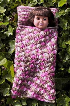 a doll is laying in a crocheted blanket on top of some leaves and bushes