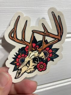 a hand holding a sticker with a deer skull and flowers on it