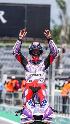 a man riding on the back of a motorcycle down a race track with his arms in the air