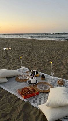 a table set up on the beach with food and drinks in front of an ocean