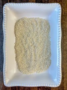 a square white plate topped with rice on top of a wooden table