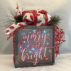 a merry and bright glass block with lights on the front is surrounded by christmas decorations